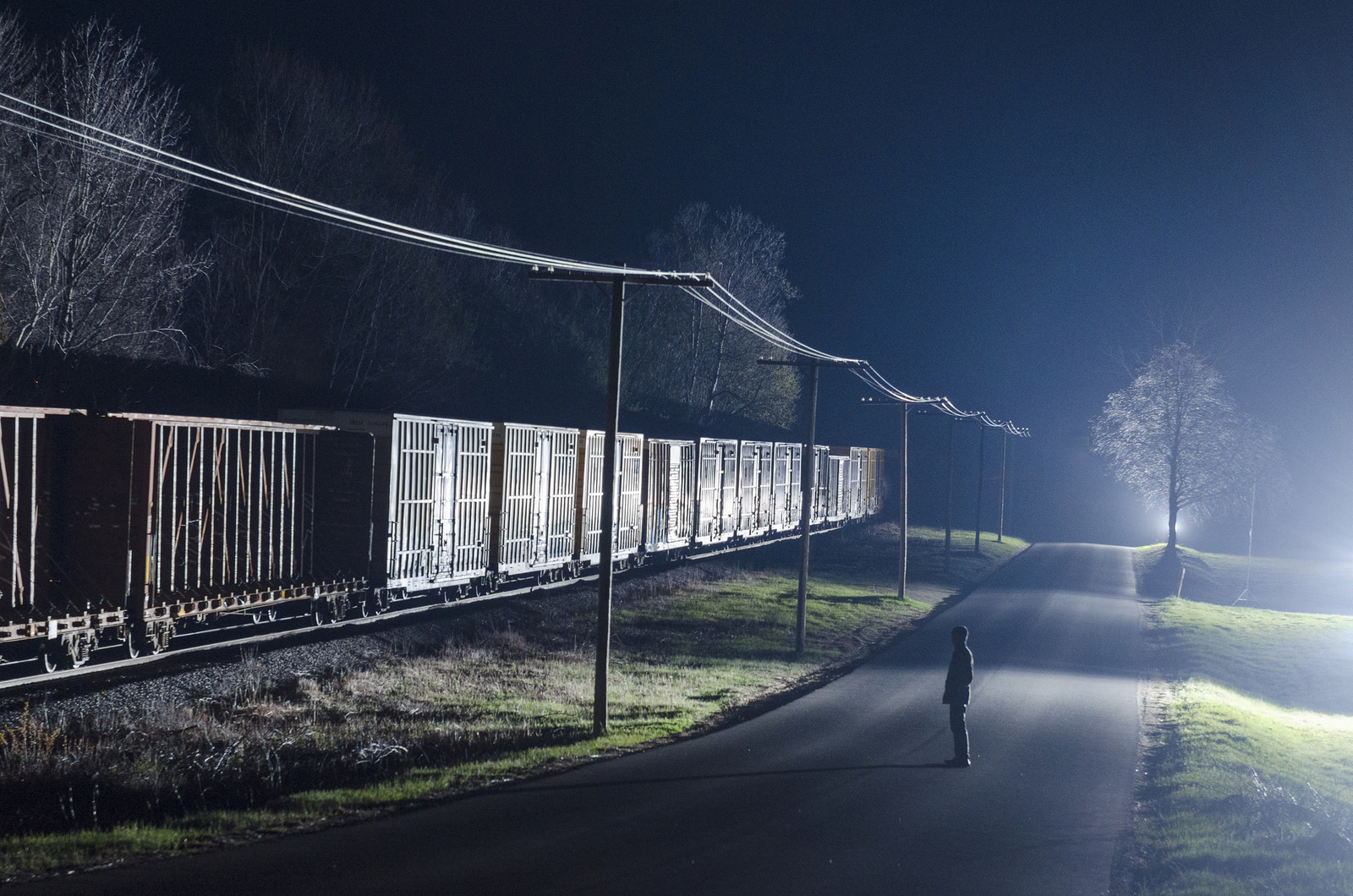 man standing in a rurual road watching freight train pass at night